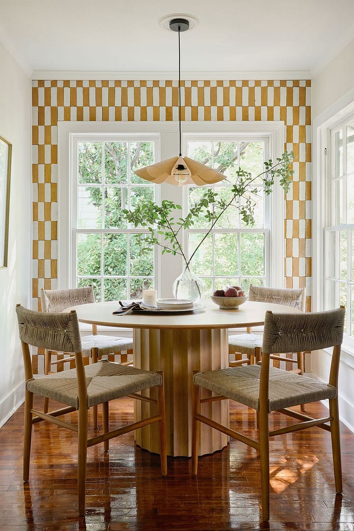 a dining room designed by joanna gaines for mini reni that has checkerboard yellow and white zellige tile and a round wood table