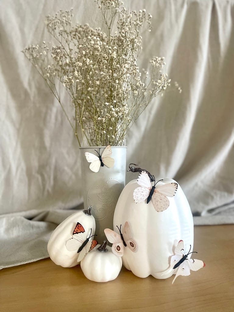 a fall centerpiece with dried flowers, white pumpkins, and paper butterflies